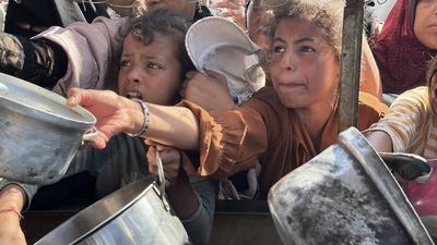 Palestinians wait in long queues to receive pots of food distributed by charitable organizations, as they face food crisis-stock-photo