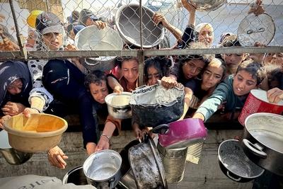 Palestinians wait in long queues to receive pots of food distributed by charitable organizations, as they face food crisis-stock-photo