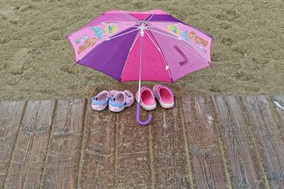 Das schlechte Wetter ist vorbei. Kinder haben am Strand den Regenschirm sch?tzend ?ber ihre Schuhe gestellt. Cavallino-T-stock-foto