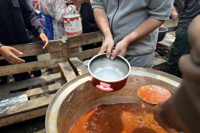 Internally displaced Palestinians gather in a charity kitchen to receive limited rations amid a shortage of food-stock-foto
