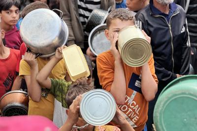 Internally displaced Palestinians gather in a charity kitchen to receive limited rations amid a shortage of food-stock-foto