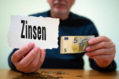 Munich, Bavaria, Germany - February 27, 2025: PHOTOMONTAGE. A man holds a sign with the word interest and a 5 euro bill-stock-foto