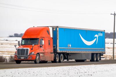 Banff, Alberta, Kanada. 2. April 2025. Ein orangefarbener Amazon Prime-Sattelschlepper f?hrt auf einer verschneiten Stra?e durch eine l?ndliche Landschaft mit einem Strommast im Hintergrund.-stock-photo