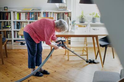 IMAGO Creative: Fr?hjahrsputz Symbolfoto zum Thema ungesunde Haltung bei der Hausarbeit. Eine alte Frau saugt mit gebeug-stock-photo