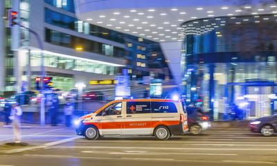 Rettungswagen des Deutsche Rotes Kreuz mit Notarzt. Auto bei Nacht vor urbaner Umgebung mit moderner Architektur, Mitzie-stock-foto