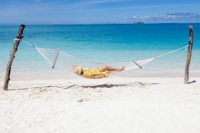 A young woman in a straw hat and a summer dress is lying in a hammock near the ocean.-stock-foto