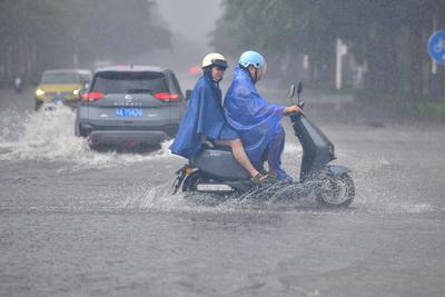 DONGFANG, CHINA - JUNE 14: A local resident rides an electric bicycle on a flooded road following the impact of Typhoon-stock-photo