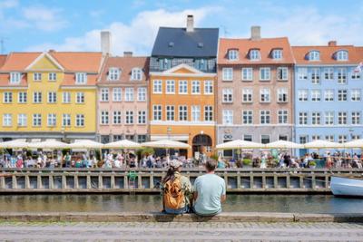 Couple Admiring Copenhagen s Colorful Waterfront A couple sits on a stone wall overlooking a bustling Copenhagen canal,-stock-photo