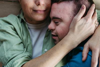 Portrait of young man with Down syndrome with his mother at home, holding, touching with foreheads. Concept of love and-stock-foto