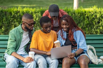 Fr?hliche Gruppe afroamerikanischer Freunde trinkt Kaffee und arbeitet an Laptops in einem gr?nen Park-stock-foto