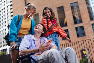 Handsome gen Z boy in a wheelchair with friends in the city. Handsome gen Z boy in a wheelchair with friends in the city-stock-photo