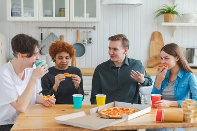 Party zu Hause. Overjoyed verschiedene Freunde essen bestellte Pizza f?r Hausparty. Gl?ckliche Gruppe multirassischen jungen Kumpels genie?en freie Wochenende Zeit zusammen Spa? lachend scherzend kommunizieren zu verbringen.-stock-photo