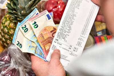 Bavaria, Germany - November 29, 2024: A man holds a shopping list with an amount over 100 euros and several euro cash bi-stock-foto