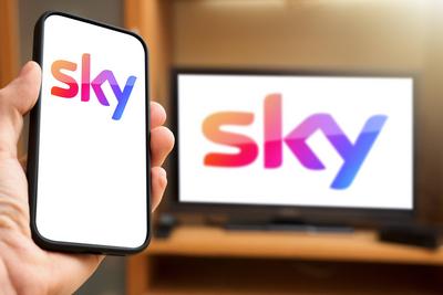 6 April 2024: Hand holding smartphone in front of TV screen with the Sky pay TV and streaming provider logo. PHOTOMONTAG-stock-foto
