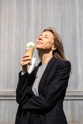 L?chelnde Frau, die ein Eis in einer Waffel genie?t und sich an den Strahlen der warmen Sommersonne erfreut, Sonnenlicht.-stock-photo