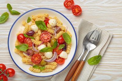 Italienischer Nudelsalat mit Fusilli, Kirschtomaten, Mozzarella, Oliven, Basilikum auf wei?em Holzhintergrund von oben, italienische K?che-stock-foto