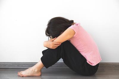 Ein trauriges junges M?dchen von 7-8 Jahren in einem rosa Hemd sitzt auf dem Boden, umarmt ihre Knie und vergr?bt ihr Gesicht, was Einsamkeit, Depression und emotionale Not symbolisiert.-stock-foto
