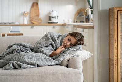 Trauriges Teenager-M?dchen, das in eine Decke eingewickelt auf der Couch liegt und ?ber Schulprobleme nachdenkt, wenn es allein zu Hause ist.-stock-photo