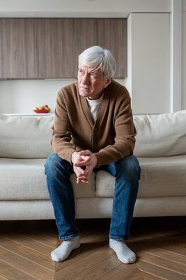Einsamer, verlassener ?lterer Mann sitzt gedankenverloren auf dem Sofa mit verschr?nkten Armen, depressiver Ged?chtnisverlust-stock-foto