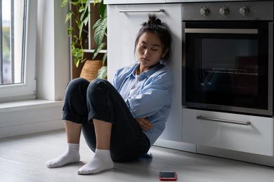 Beleidigte, ungl?ckliche asiatische Frau, die traurig auf ihr Telefon schaut, sitzt auf dem Boden, nachdem sie sich von ihrem Freund getrennt hat-stock-photo