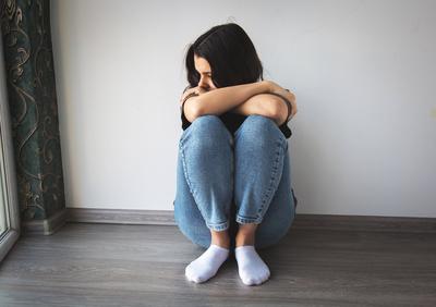 Eine auf dem Boden sitzende Frau, die ihre Knie umarmt und mit traurigem Gesichtsausdruck wegschaut, symbolisiert Einsamkeit, Depression und emotionale Bedr?ngnis-stock-foto
