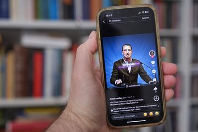 Hand h?lt ein Mobiltelefon auf dessen Display die Seite des rechtsextremen AFD Politikers Matthias Helferich auf der Plattform TikTok  zu sehen ist *** Hand holds a mobile phone on whose display the page of the right-wing extremist AFD politician Matthia-stock-foto