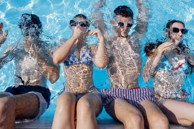 Cute teens in swimsuits and sunglasses in the pool. Smiling boys and girls dive into the clear water. Cute teens in swim-stock-foto