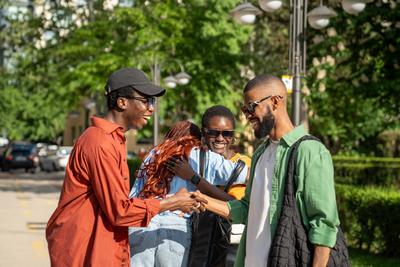 Fr?hliche, fr?hliche afroamerikanische Freunde, die ein pl?tzliches, angenehmes Treffen auf der Stra?e im Freien genie?en-stock-foto