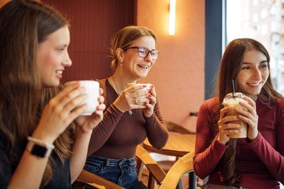 Junge M?dchen lachen und trinken k?stliche Kaffeegetr?nke in einem Caf?. Die Freunde halten Gl?ser mit Milchshakes und Cocktails und haben Spa? zusammen. Studenten essen und chatten-stock-photo