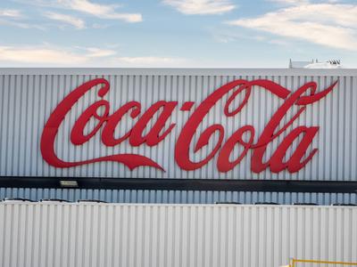 Ein gro?es, rotes Coca-Cola-Logo prangt auf einem wei?en Geb?ude mit vertikalen Streifen unter einem teilweise bew?lkten Himmel.-stock-foto