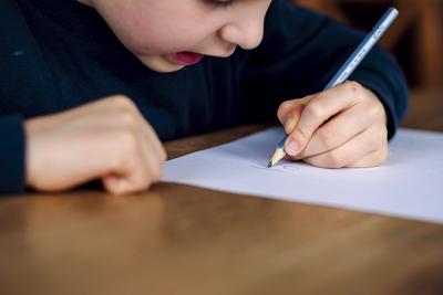Symbolfoto zum Thema Linkshaender: Ein fuenfjaehriger Junge sitzt zu Hause und schreibt mit einem Bleistift in der linke-stock-foto