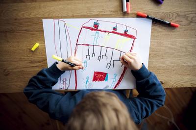 Symbolfoto zum Thema Kreativitaet bei kleinen Kindern: Ein fuenfjaehriger Junge sitzt zu Hause und malt mit Buntstiften-stock-foto