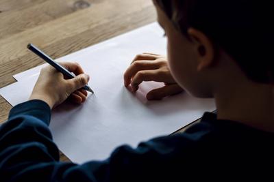 Symbolfoto zum Thema Linkshaender: Ein fuenfjaehriger Junge sitzt zu Hause und schreibt mit einem Bleistift in der linke-stock-foto