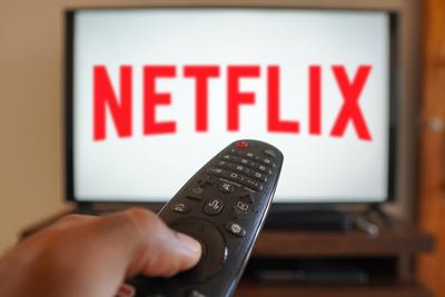 April 20, 2024, Brazil. In this photo illustration, a hand holding a TV remote control in front of the Netflix logo on a-stock-foto