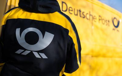 Eine Postbotin tr?gt vor einem Zustellfahrzeug eine Jacke mit dem Logo der Deutschen Post. Rottweil Baden-W?rttemberg De-stock-foto