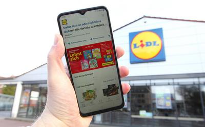 Ein Mann h?lt vor einer Filiale vom Discounter-Konzern LIDL ein Smartphone in der Hand. Darauf wurde die App von LIDL ge-stock-foto