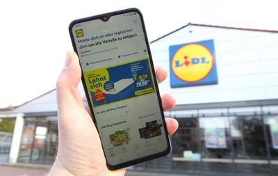 Ein Mann h?lt vor einer Filiale vom Discounter-Konzern LIDL ein Smartphone in der Hand. Darauf wurde die App von LIDL ge-stock-foto