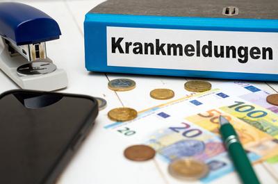 Augsburg, Bavaria, Germany - November 13, 2023: Folder with sick notes on a desk next to euro coins and banknotes PHOTOM-stock-foto