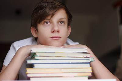 Ein Jugendlicher st?tzt sich auf einen Stapel Schulb?cher und schaut traurig in Gedanken-stock-foto