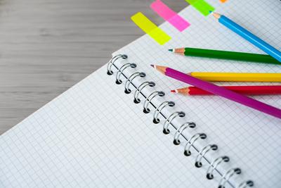 Buntstifte auf einem Teil eines Spiralheftes und bunte Marker auf einem grauen Schreibtisch, kreatives Arbeiten oder Schulmaterial, Kopierraum, ausgew?hlter Fokus-stock-foto