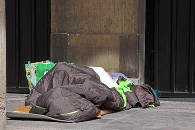 Armutsschicksale in Deutschland Eine von Obdachlosigkeit betroffenen Person liegt in einem Schlafsack vor dem Portal der-stock-foto