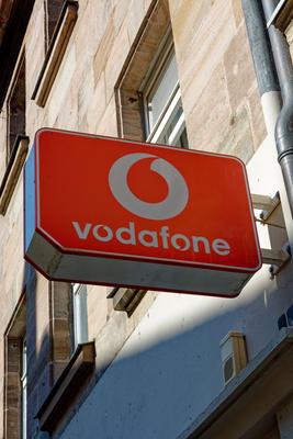 Schild mit dem Symbol des Unternehmens Vodafone an einer Hausfassade *** Shield with the symbol of Company Vodafone to a-stock-foto