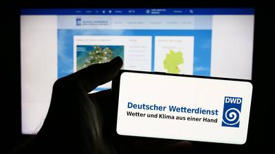 Person holding mobile phone with logo of German meteorological service Deutscher Wetterdienst (DWD). Stuttgart, Germany-stock-foto