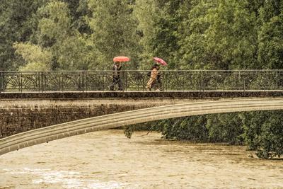 Isar-Hochwasser, Meldestufe 1, Passanten mit leuchtend bunten Regenschirmen fl?chten auf dem Kabelsteg vor dem Wolkenbruch, M?nchen, 29. Juli 2025-stock-foto