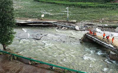 LUANPING, CHINA - JULY 29: Rescuers carrying construction materials wade through a river to build a temporary bridge on-stock-foto