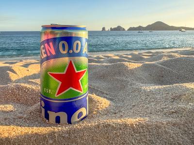 Los Cabos, B.C.S, Mexiko. 29. Dezember 2024. Eine Heineken 0,0%-Bierdose liegt im Sand, mit Blick auf einen malerischen Strand mit Booten am Horizont und einem atemberaubenden Sonnenuntergang.-stock-foto