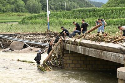 LUANPING, CHINA - JULY 29: Rescuers carrying construction materials wade through a river to build a temporary bridge on-stock-foto