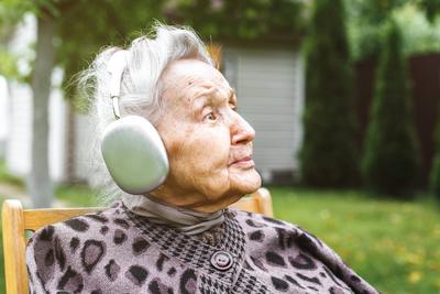 ?ltere Frau mit Kopfh?rern sitzt auf einem Stuhl im Freien und genie?t Musik, Konzept des Alterns und der modernen Technologie-stock-foto