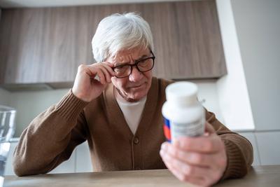 Elderly man squints reading medication label through glasses showing distrust and confusion-stock-foto