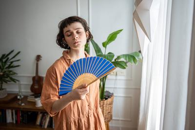 Traurige, m?de Frau mit Ventilator, die den extremen Sommerbedingungen ausgesetzt ist. Hitzeersch?pfung und Frustration-stock-foto